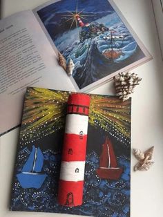 an open book with a lighthouse on it next to some sea shells and seashells