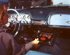 a woman sitting in the driver's seat of a classic car with dashboard lights on