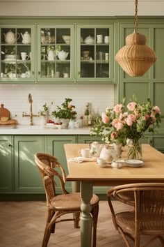 a kitchen with green cabinets and flowers in vases on the dining room table, along with wicker chairs