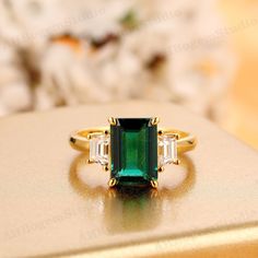 an emerald and diamond ring sitting on top of a gold box