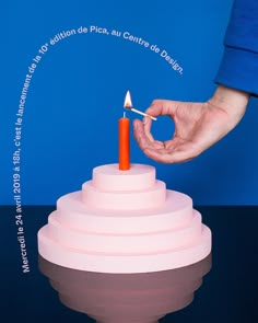 a person lighting a candle on top of a pink cake that is stacked in the shape of a pyramid