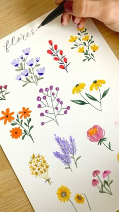 a person is drawing flowers on a piece of paper with watercolors and ink