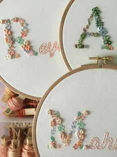 three embroidered hoops with letters and flowers on them next to thread spools