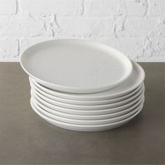 a stack of white plates sitting on top of a table next to a brick wall