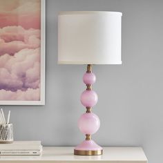 a pink lamp sitting on top of a white table next to a framed photo and books