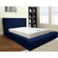 a bed with a blue velvet headboard and foot board in a living room next to a bookshelf