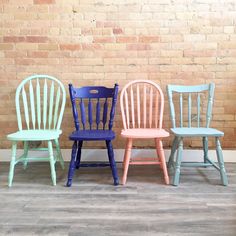 three different colored chairs sitting in front of a brick wall