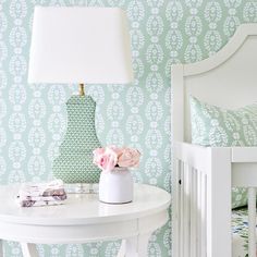 a white table with a flower vase on it next to a lamp and wallpaper