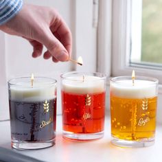 three different colored candles sitting next to each other on a window sill in front of a person's hand