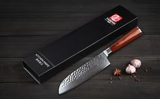 the knife is next to some garlic and an open box on a wooden table with cloves