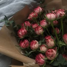 a bunch of pink flowers sitting on top of a brown paper bag with green leaves