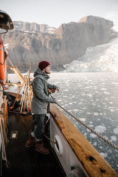 a man standing on the deck of a boat looking out at icebergs in the water