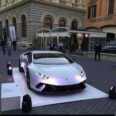 a white sports car on display in front of a building with people walking around it