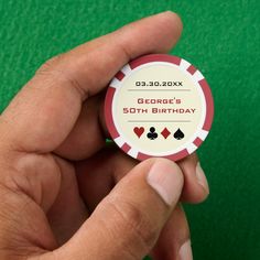 a hand holding a red and white poker chip with the words george's 50th birthday on it