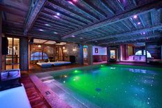 an indoor swimming pool surrounded by stone walls and wooden beams with lights on the ceiling