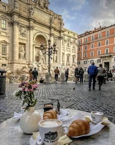 there is a plate with croissants and coffee on the table in front of an old building