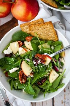 a salad in a bowl with apples and crackers next to it on a table