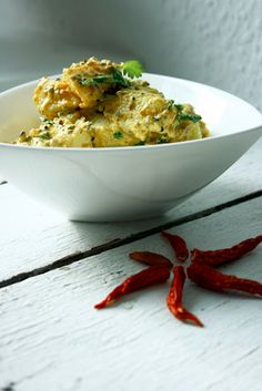 a white bowl filled with food sitting on top of a wooden table next to red chili peppers