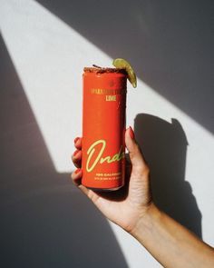 a person holding up a can of soda with a lime slice on the top of it