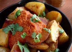 a black bowl filled with potatoes and meat covered in sauce, garnished with cilantro