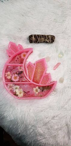 a pink purse with flowers on it sitting on a white fur covered surface next to a stick