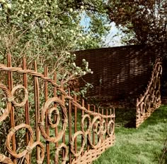 an iron fence made out of bamboo sticks in the grass next to a brick wall