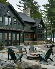 an outdoor fire pit in front of a house with lawn chairs and rocks around it