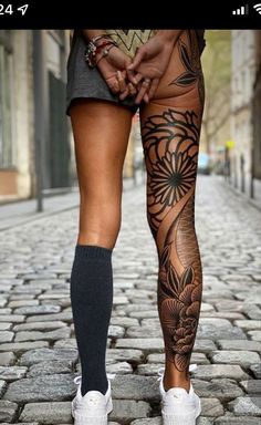 a person with tattoos on their legs walking down a cobblestone street in the city