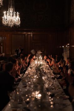 many people are sitting at a long table with wine glasses on it and candles in the middle