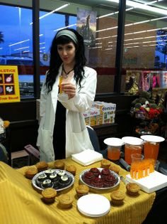 a woman standing in front of a table filled with cupcakes and pastries