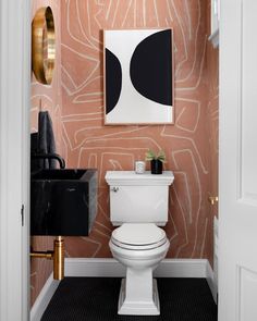 a white toilet sitting next to a sink in a bathroom under a painting on the wall