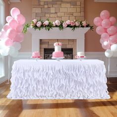 a table topped with pink and white balloons next to a fire place filled with cake