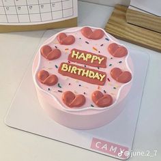 a birthday cake with pink frosting and hearts on it sitting on a desk next to a calendar