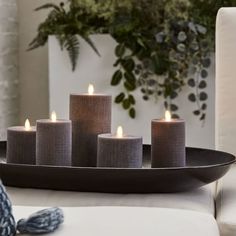 five candles are lit on a tray in front of a chair and potted plant