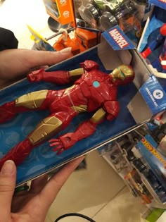 a hand holding a toy in a box with other toys on the shelf behind it