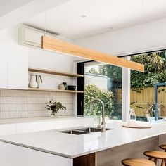 a kitchen with white counter tops and wooden stools in front of a large window