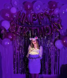 a woman holding a birthday cake in front of balloons