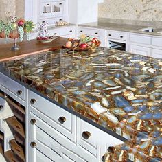 a kitchen with marble counter tops and white cabinets in the background, along with an island that has fruit on it