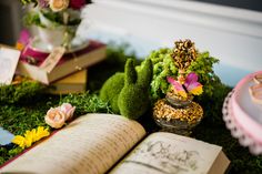 an open book sitting on top of a lush green field next to flowers and plants