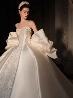 a woman in a white wedding dress with a large bow around her neck and shoulder