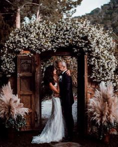 a bride and groom are standing in front of an archway with flowers on the sides