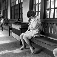 a black and white photo of a woman sitting on a bench in an old hospital