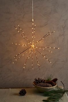 a star shaped light hanging from the ceiling next to a bowl with pine cones on it