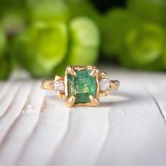 an emerald and diamond ring sitting on top of a table