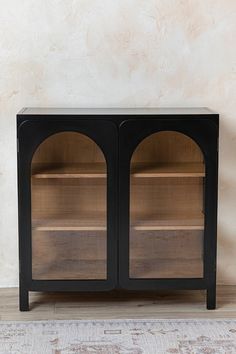 a black cabinet with two glass doors on the top and bottom, in front of a beige wall