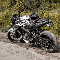 the motorcycle is parked on the side of the road near some bushes and trees in the background