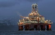 an oil rig in the middle of the ocean at night with lights shining on it