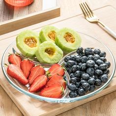 a plate filled with sliced kiwis, strawberries and blueberries on top of a wooden cutting board