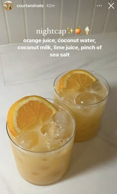 two glasses filled with orange juice sitting on top of a table next to each other