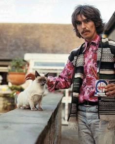 a man standing next to a white cat on top of a cement wall near a building